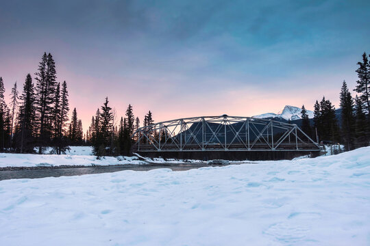Sunrise over snowy rocky muntains and the bridge cross the river in pine forest on winter at Banff national park