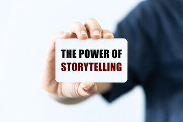 The power of storytelling text on blank business card being held by a woman's hand with blurred background. Business concept about storytelling.