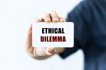 Ethical dilemma text on blank business card being held by a woman's hand with blurred background. Business concept about ethics.