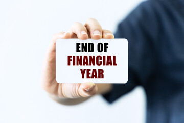 End of financial year text on blank business card being held by a woman's hand with blurred background. Business concept about end financial period.