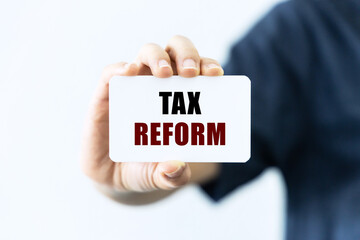 Tax reform text on blank business card being held by a woman's hand with blurred background. Business concept about tax reform.