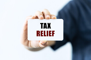 Tax relief text on blank business card being held by a woman's hand with blurred background. Business concept about tax relief.