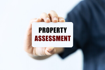Property assessment text on blank business card being held by a woman's hand with blurred background. Business concept about property assessment.