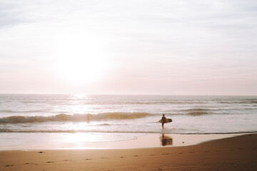 Fototapeta na wymiar Silueta de surfista entrando en el agua al atardecer en playas de andalucia