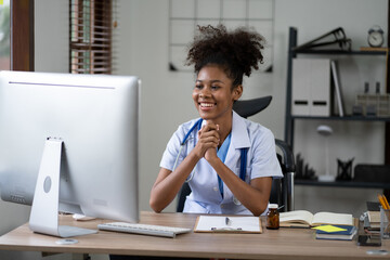 Portrait of female African American doctor sitting in her office at clinic. working with dewsktop computer.