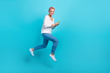 Fototapeta na wymiar Full length photo of young careless girl jumping running fast hold her new smartphone fast wifi connection ad isolated on aquamarine color background