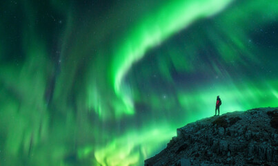 Northern lights and young woman on mountain peak at night. Aurora borealis and silhouette of alone...