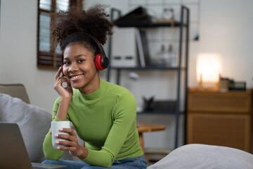 Fototapeta premium Pretty African American woman relaxing at her home using laptop and drinking a cup of coffee.