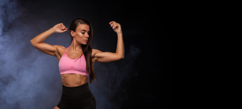 Beautiful fitness girl. Woman in shorts and pink sportswear. Black background with smoke. A high resolution. Photo for advertising