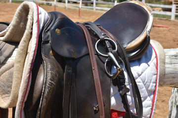 A traditional Asian saddle and its equipments standing on the fence in the horse farm. Traditional horseback riding
