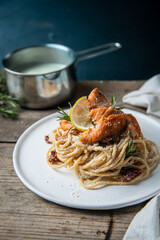 Homemade pasta with baked salmon bites, sun dried tomatoes and creamy lemon sauce on white plate on rustic wooden table.