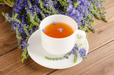 Healthy herbal tea in a white cup on a brown wooden background with Veronica's blue bouquet