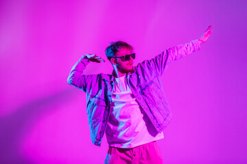 Fashion handsome man dancer with sunglasses in casual stylish denim clothes dance in creative colorful studio with pink and neon light color