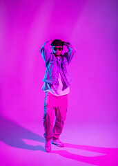 Fashionable male dancer in stylish clothes dancing in a creative studio with pink and neon lights