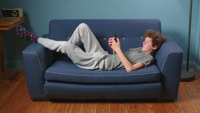 Teenager sits on the couch without talking. Boy addicted to gadgets, using mobile phone, laptop at home. Internet obsession concept