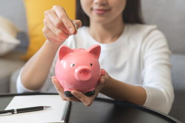 Saving money wealth concept, asian young business woman hand putting coin into piggy for saving...