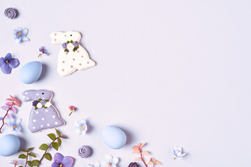 Easter background. Easter decorations, bunny, eggs and flowers on violet background. Copy space, flat lay. Corner frame.