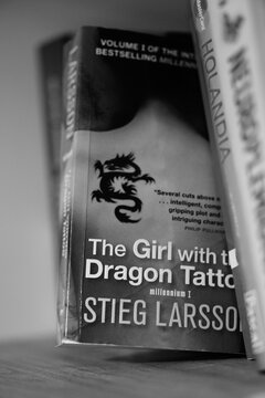 Vertical grayscale closeup of Stieg Larsson's The Girl With The Dragon Tattoo novel on a shelf.