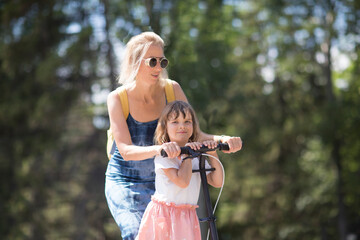 mom and child daughter ride a scooter in the park in summer. happy family has fun together in nature © ulza