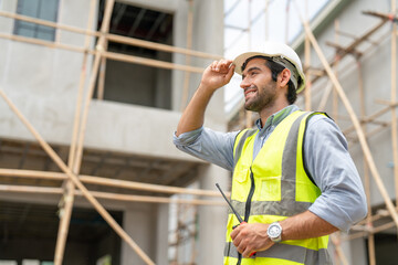 Portrait of male civil engineer wear safety vest with white helmet holding walkie talkie walking to inspection housing estate at construction site