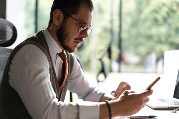 Smiling businessman holding smartphone sitting in office. Middle aged manager ceo using cell phone mobile apps