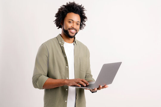 Smiling positive man holding laptop in hands and typing. Blogger making posts in social networks, chatting with followers. Indoor studio shot isolated on white background