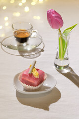 a pink petit four, a pink tulip ,and an espresso cup in the backtrop are the objects in bright light