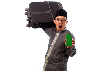 Asian muslim man holding suitcase while showing blank cell phone display. Homecoming concept. Selective focus