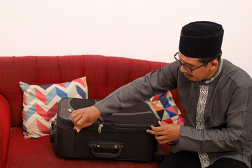 Asian muslim man sitting on the sofa while checking his suitcase