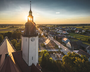 wieża kościoła z blaskiem zachodzącego słońca z promieniami i widokiem wsi opolskiej w Polsce