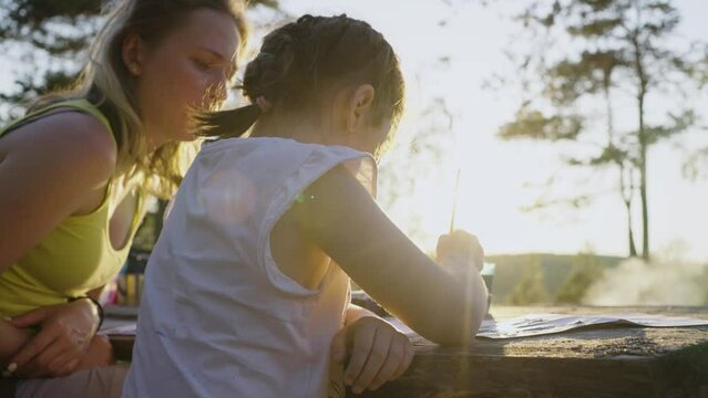 Homeschooling in nature, a young mother with her daughter paint with a brush in nature at sunset, free learning home education