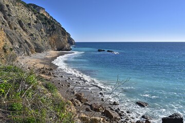 Fototapeta na wymiar View of Praia da Mijona Beach and blue sea surrounded by rocky hills under clear sky in Portugal