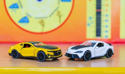 Two toy models of sports cars stand on wooden table against blurred color background.