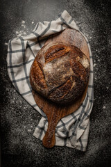 Top view of a freshly baked bread on a wooden board on a black table
