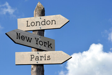 London, New York, Paris - wooden signpost with three arrows, sky with clouds