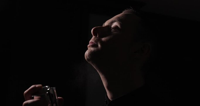 Man spraying perfume on his neck, slow motion, black dark background