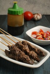 Maranggi satay on white plate over dark background with tomato and Indonesia sweet soy dipping sauce (sambal kecap)