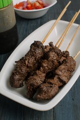 Maranggi satay on white plate over dark background with tomato and Indonesia sweet soy dipping sauce (sambal kecap)