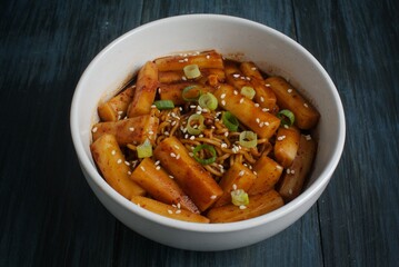 Rapokki or rabokki stand for ramyeon and teokpokki, a korean rice cake mix with instan noodles garnish with sesame seed and cut chives. Isolated in dark blue background
