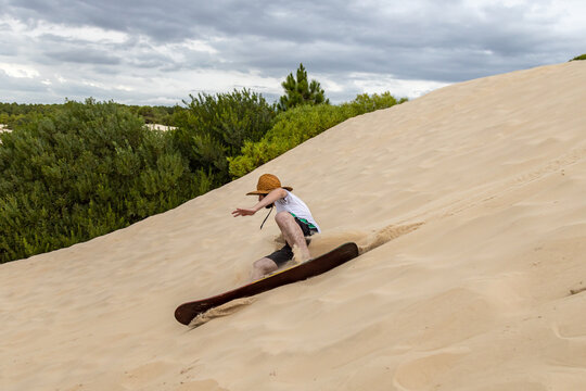 Man riding a sandboard wearing a straw hat, shorts and white shirt on Rio Grande do Sul coast, Brazil