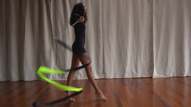 Attractive slim teen girl rhythmic gymnast wearing black sports clothes training exercise with ribbon