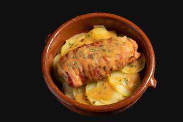 Chicken breast stuffed with cheese wrapped with strips of bacon in its sauce, over baked potatoes in a clay pot. Concept of rich and delicious cuisine.