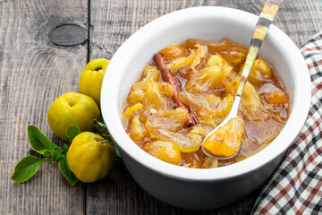 Homemade quince jam in ceramic bowl and fresh quince with leaves on wooden table
