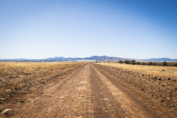 Fototapeta na wymiar A dirt road leading off into the distance to mountains on the horizon under a clear blue sky.