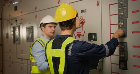 Obraz premium Two electricians electrical engineers in protective uniform checking voltage control panel screen system at electrical cabinet for generate electricity of factory in manufacture industrial