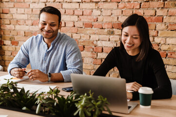 Two cheerful colleagues working together at table in coworking