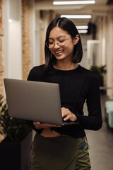 Smiling asian business woman working on laptop while standing in office