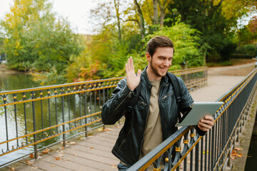 Fototapeta premium Cheerful man making video call via tablet and waving while standing in park