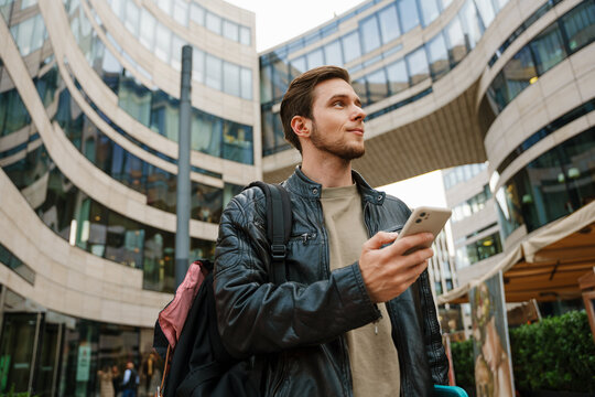 Young man using mobile phone and looking aside while standing outdoors