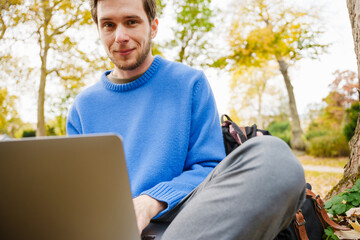 Fototapeta premium Cheerful man working on laptop while sitting in park